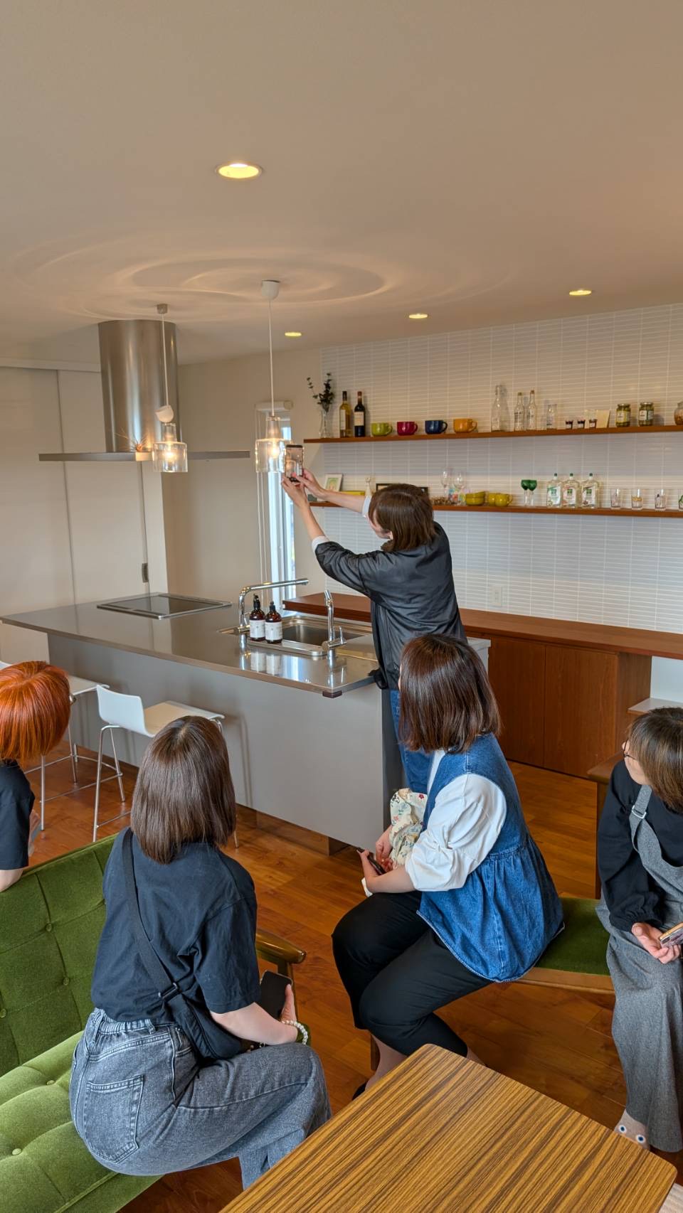 キッチンのある会場で、講師が背伸びしてスマートフォンでの撮影を実演し、参加者が見守る講座風景