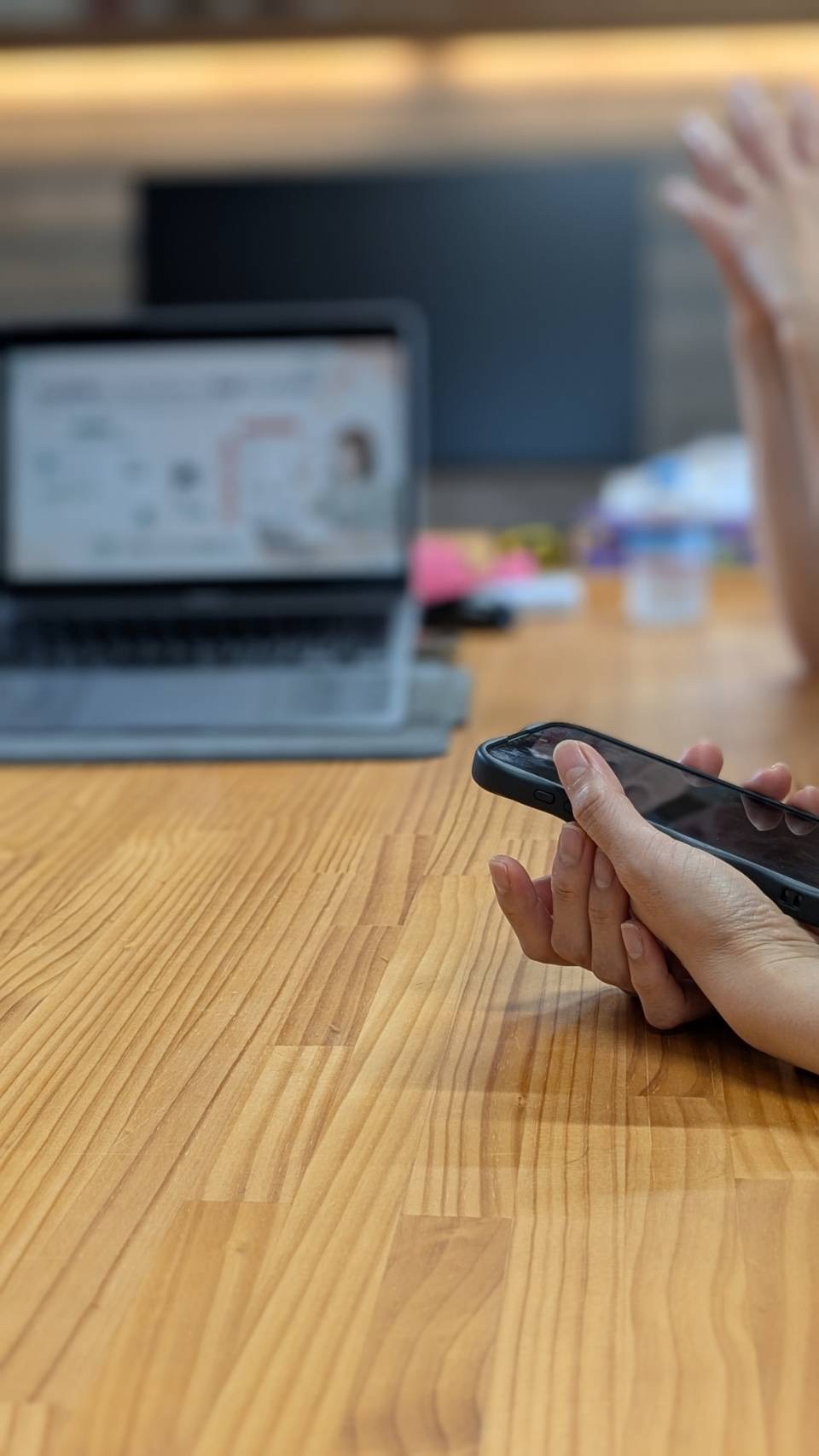 木のテーブルでスマートフォンに触れながら、そばのノートパソコンを使って学ぶ個別サポートの様子